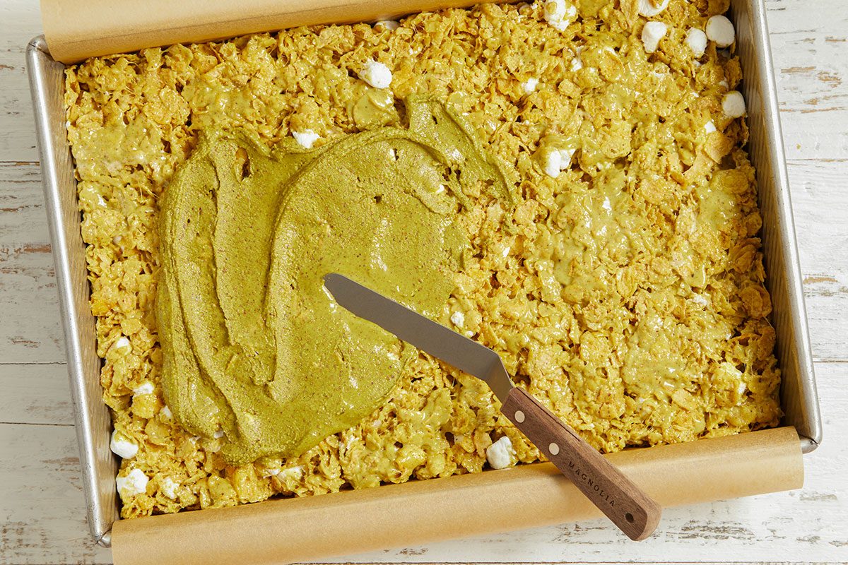 The cornflake mixture is pressed into a pan and pistachio butter is spread evenly over the top.