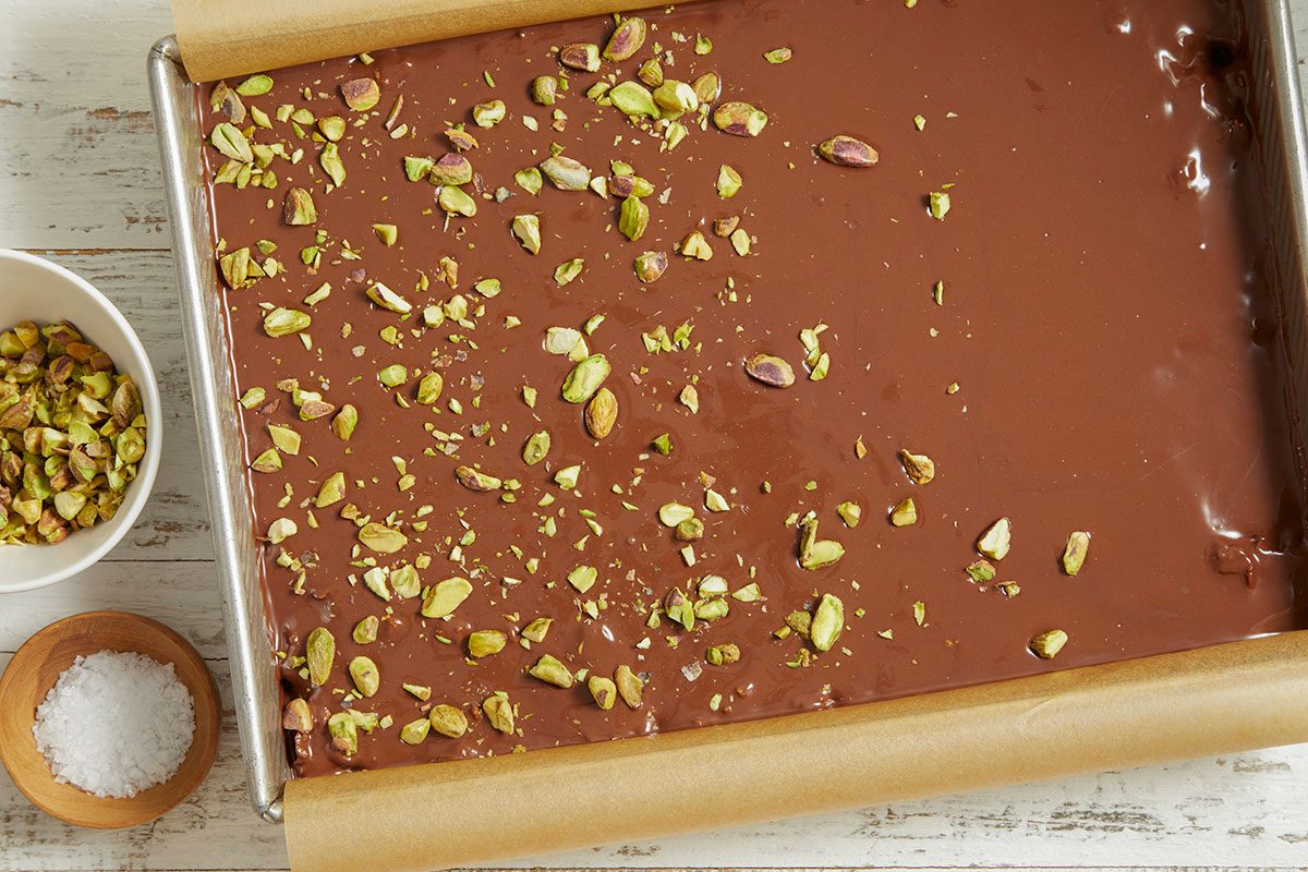 Melted chocolate is poured over the bars and topped with chopped pistachios and flaky salt.