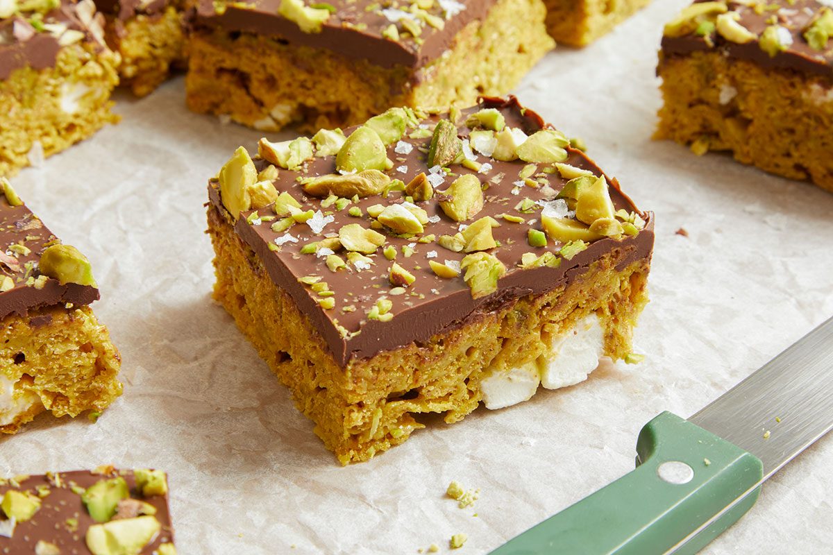 A close-up shows the layered texture of cornflakes, marshmallow, pistachio butter, and chocolate.