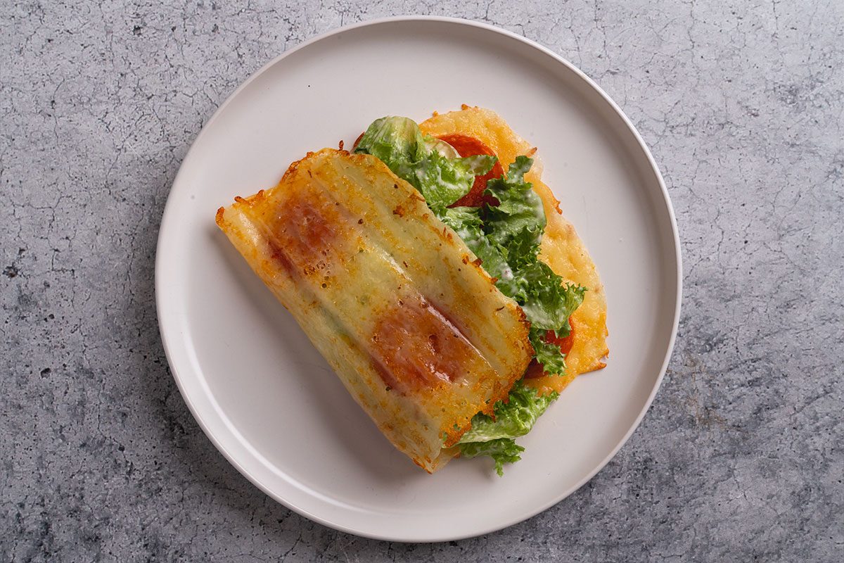 Finished pizza Caesar wrap on a white plate, filled with lettuce and dressing, with the cheesy crust folded around the filling.