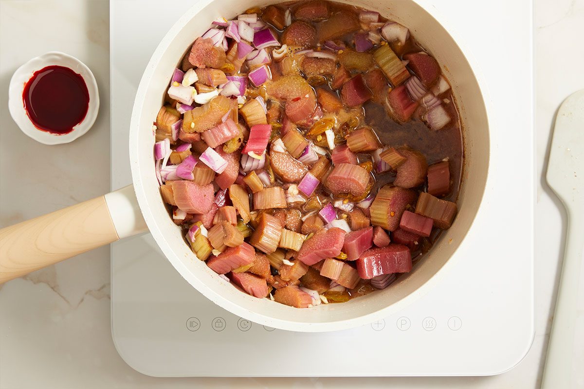 Overhead process image of chopped rhubarb, onion, and spices simmering together in saucepan.
