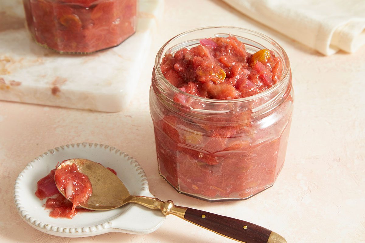 Horizontal beauty image of rhubarb chutney served in glass jar with spoon for serving.