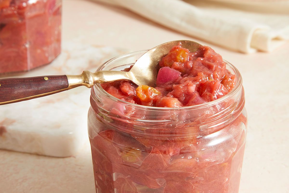 Horizontal close-up beauty image of spoon scooping rhubarb chutney from jar highlighting chunky consistency.