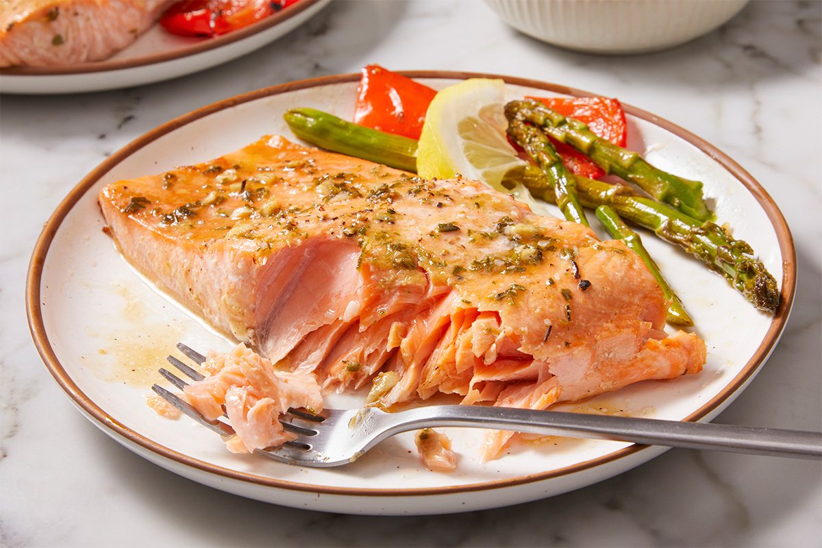 3/4 angle horizontal close-up of cooked salmon flaked with a fork, served with vegetables and lemon.