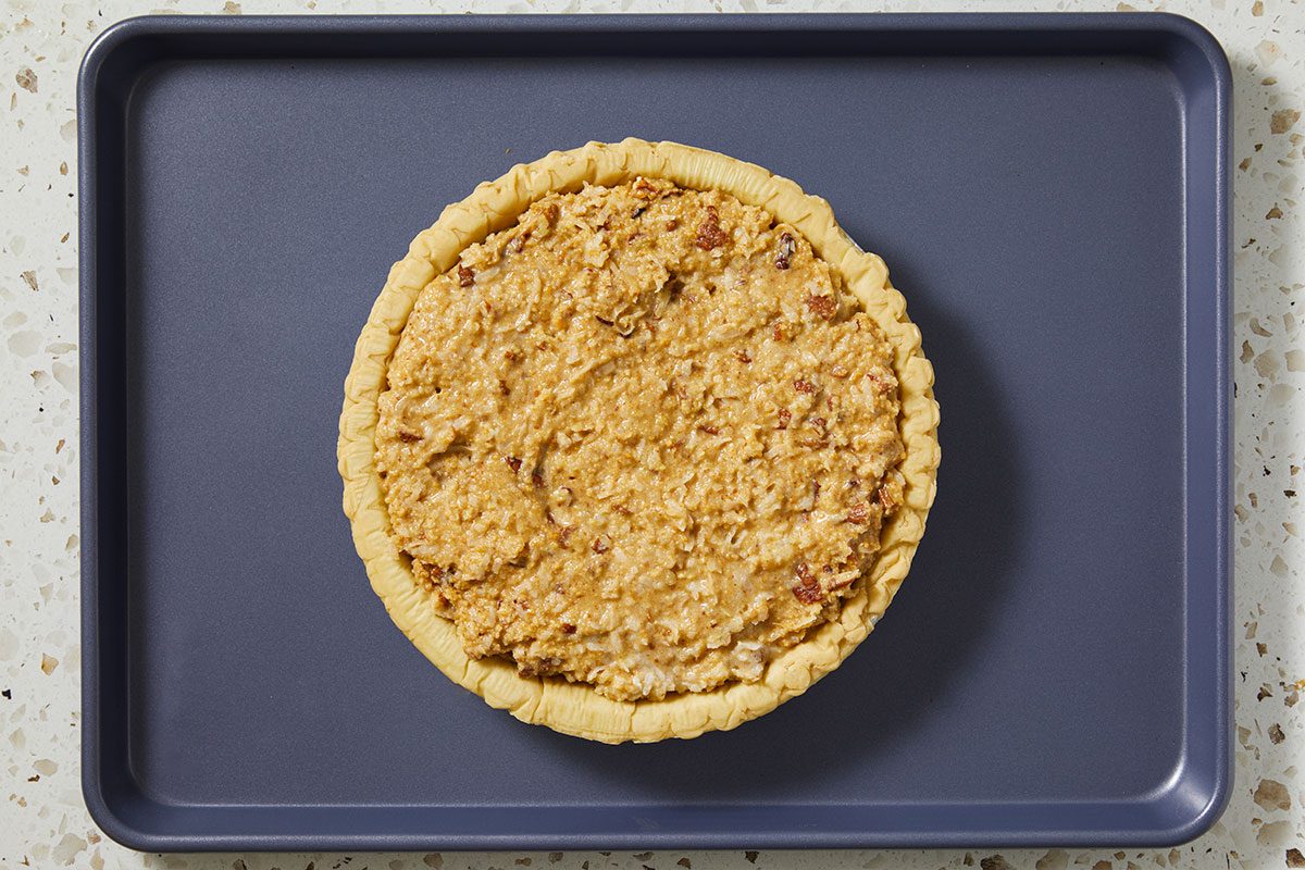 A horizontal overhead image shows an unbaked pie filled with a textured coconut and pecan mixture resting on a baking sheet.