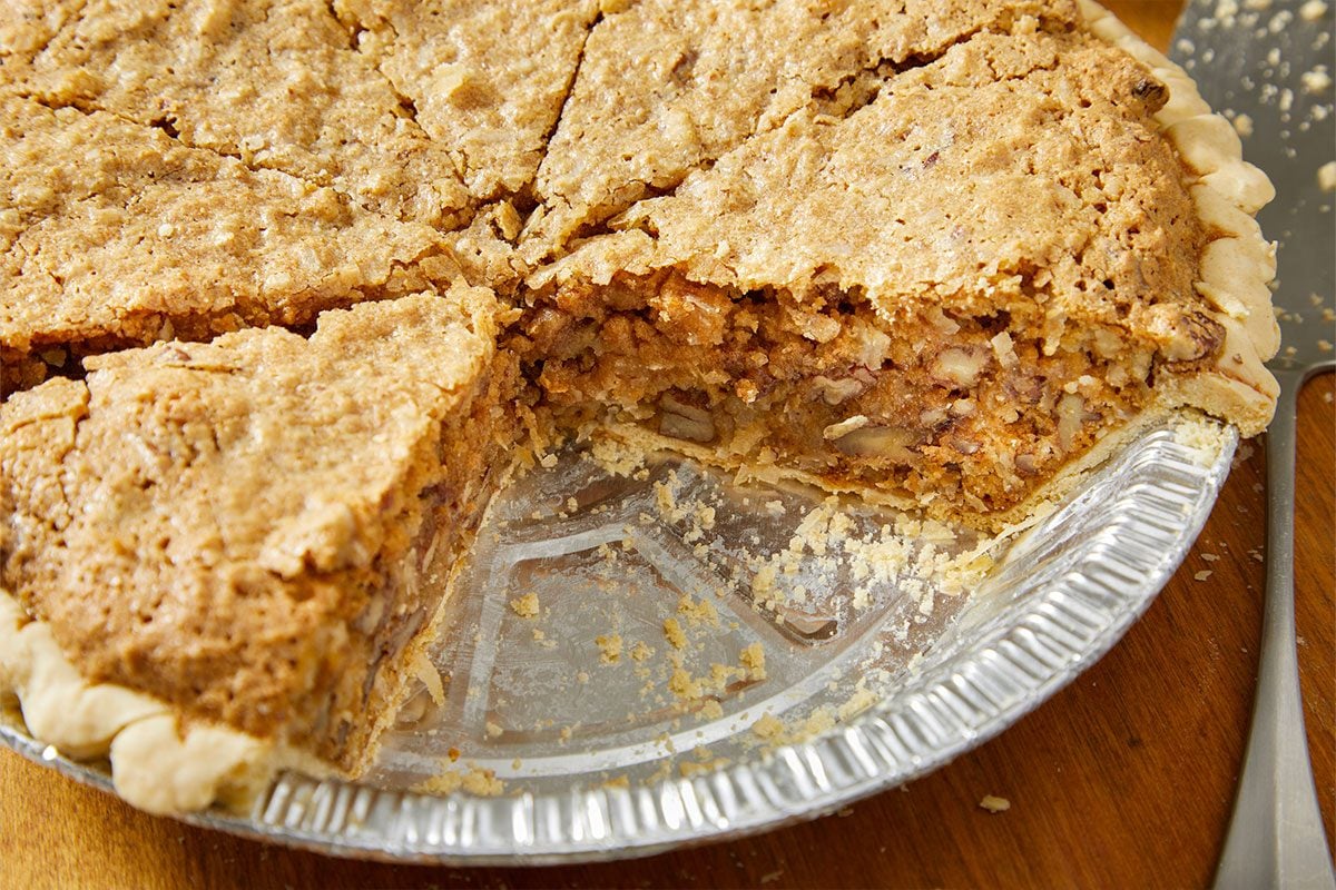 A horizontal close-up image shows a slice of sawdust pie revealing a dense, textured filling with coconut and pecans.