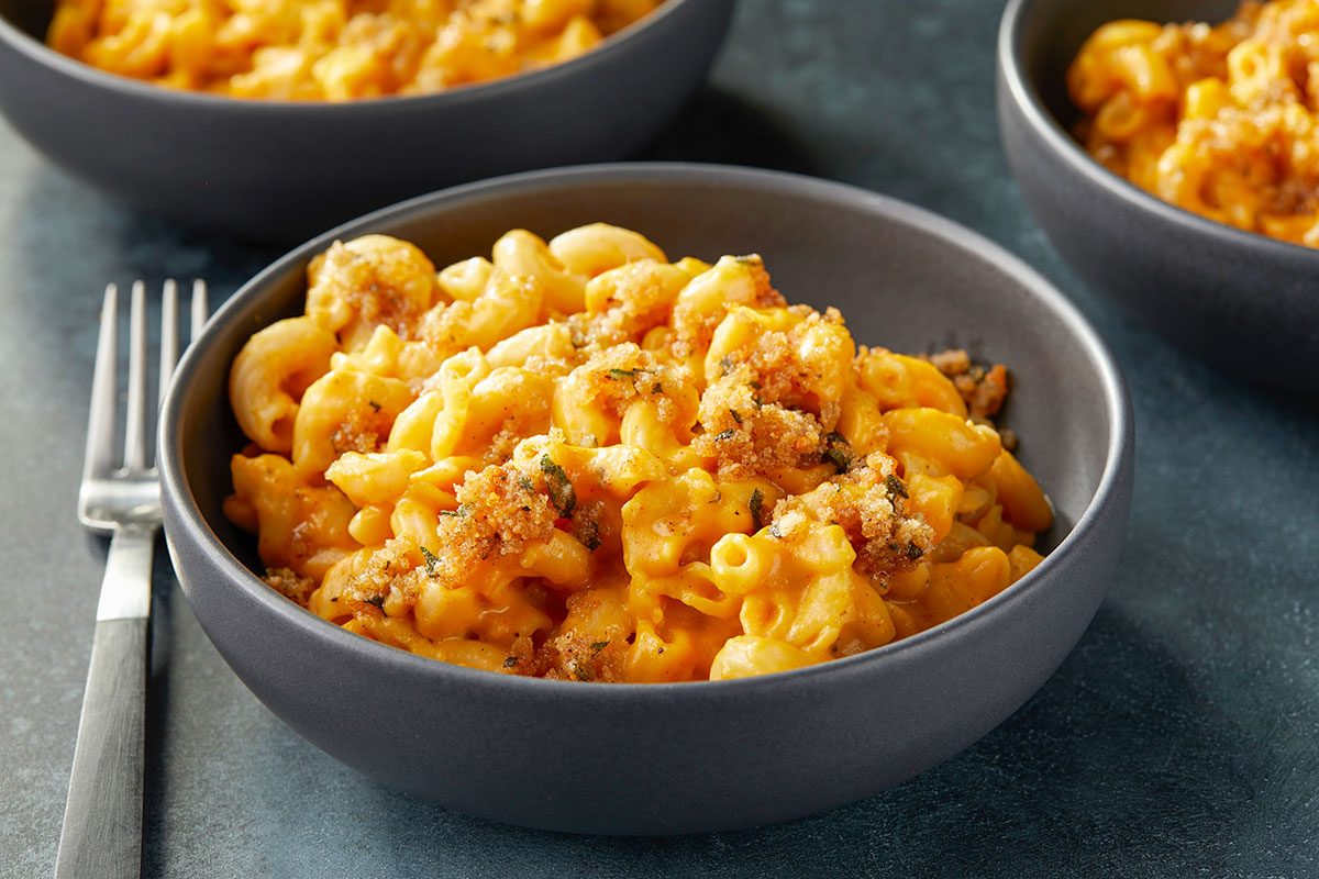 Eye-level horizontal image of a bowl of creamy pumpkin mac and cheese with crispy breadcrumb topping and herbs.