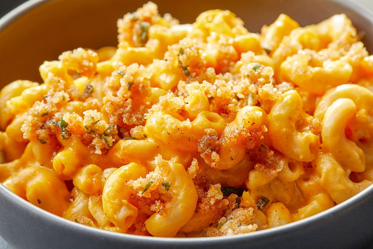 Eye-level horizontal close-up of pumpkin mac and cheese highlighting creamy sauce, pasta texture, and crispy sage topping.