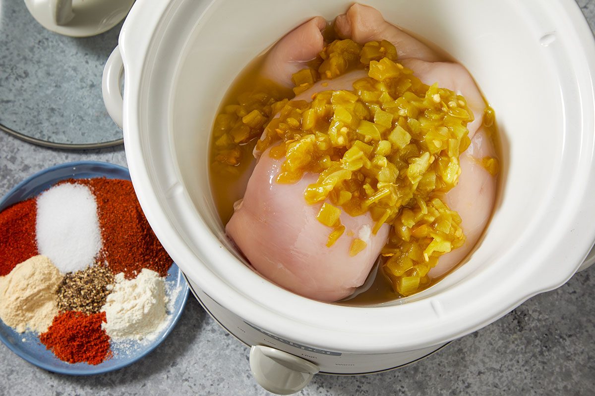 Overhead horizontal step-by-step image of raw chicken breasts in a slow cooker topped with corn, green chiles, and spices before cooking.