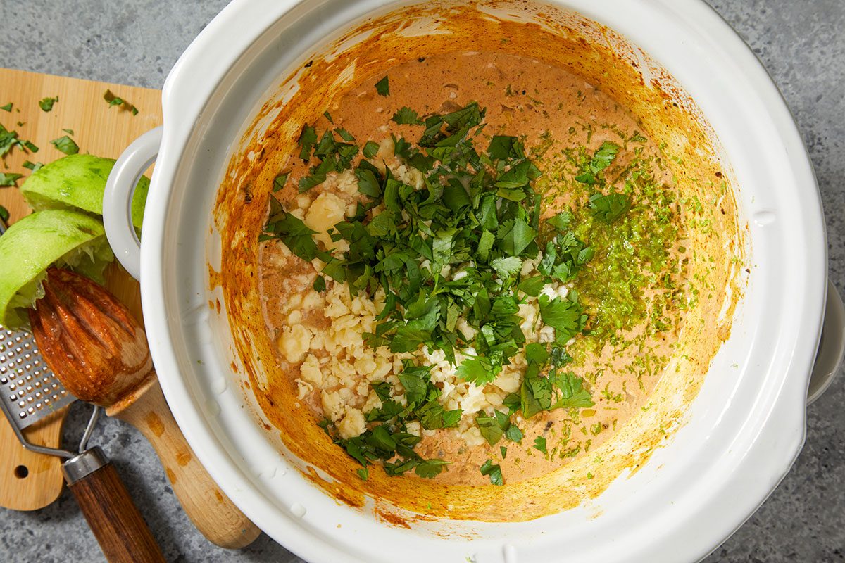 Overhead horizontal step-by-step image of cooked creamy corn chicken mixture in slow cooker being stirred with fresh cilantro.