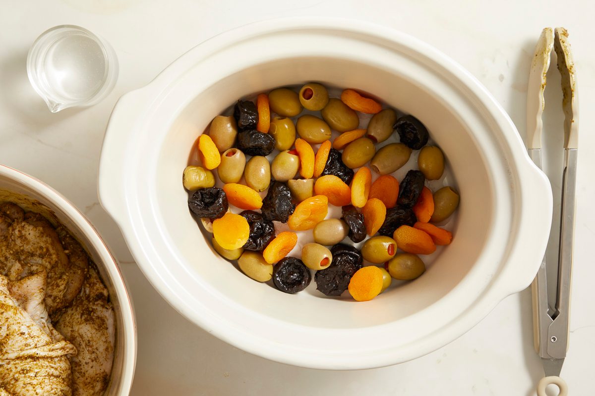 olives, apricots and plums arranged in the bottom of a slow-cooker