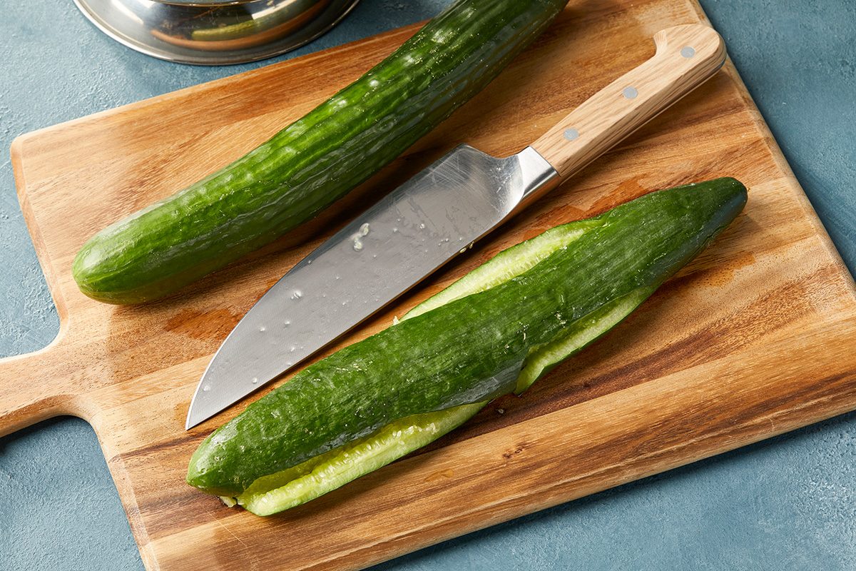 A cucumber on a wooden cutting board, partially sliced in half with a knife resting beside it.