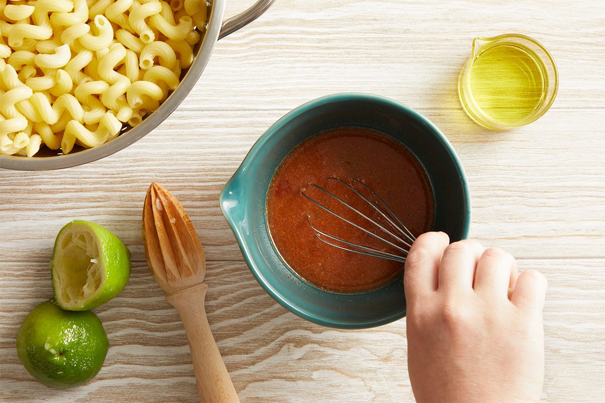 Overhead shot of a hand mixing a red dressing in a bowl with lime and olive oil on the side.