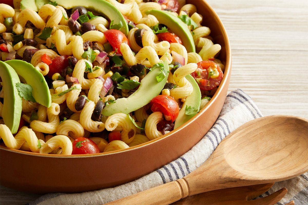 Close up shot of Southwestern Spiral Pasta being served from a large brown bowl with a wooden spoon.