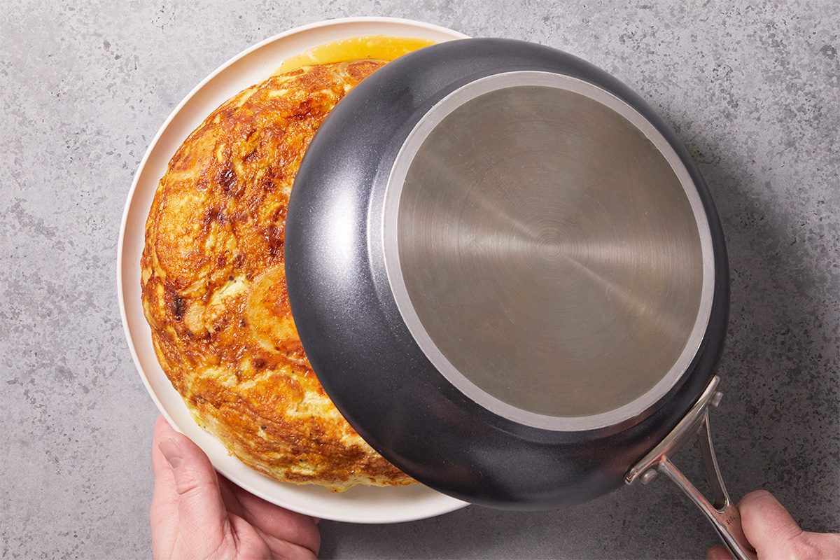 Overhead step-by-step image of the Spanish omelet being flipped from a skillet onto a plate, showing the golden cooked tortilla surface during preparation.
