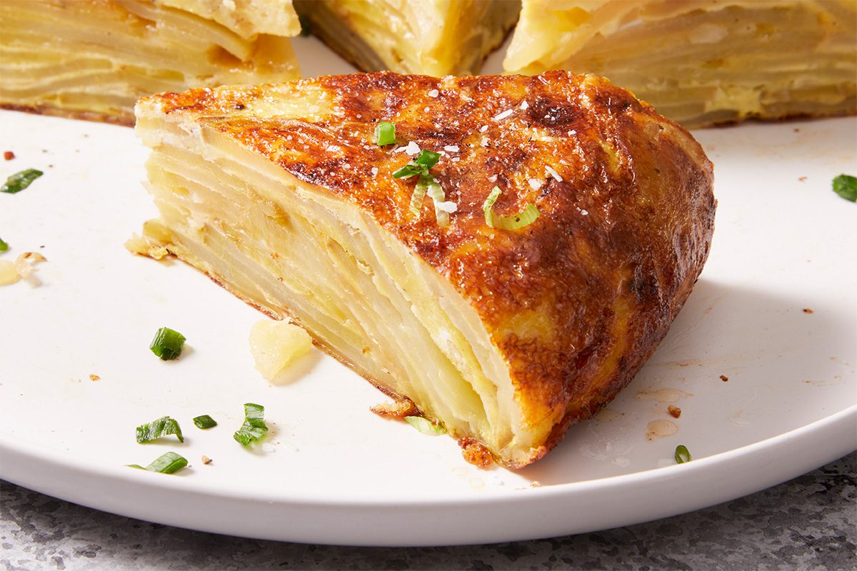 Horizontal push and pulls close-up image of a slice of Easy Spanish Omelet on a white plate, highlighting the tender layers of potatoes and eggs with a golden browned crust.