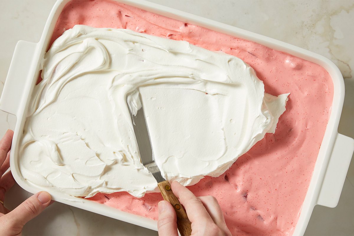 Strawberry gelatin is combined with boiling water and mixed with chopped strawberries to create a fruit layer.