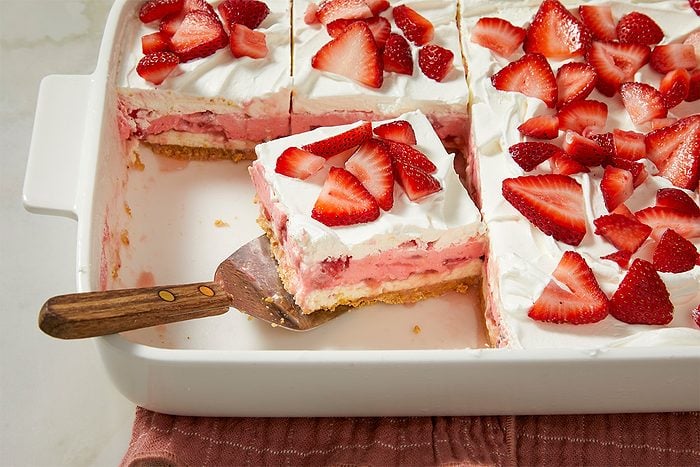 A final layer of whipped topping is spread over the dessert and topped with fresh sliced strawberries.