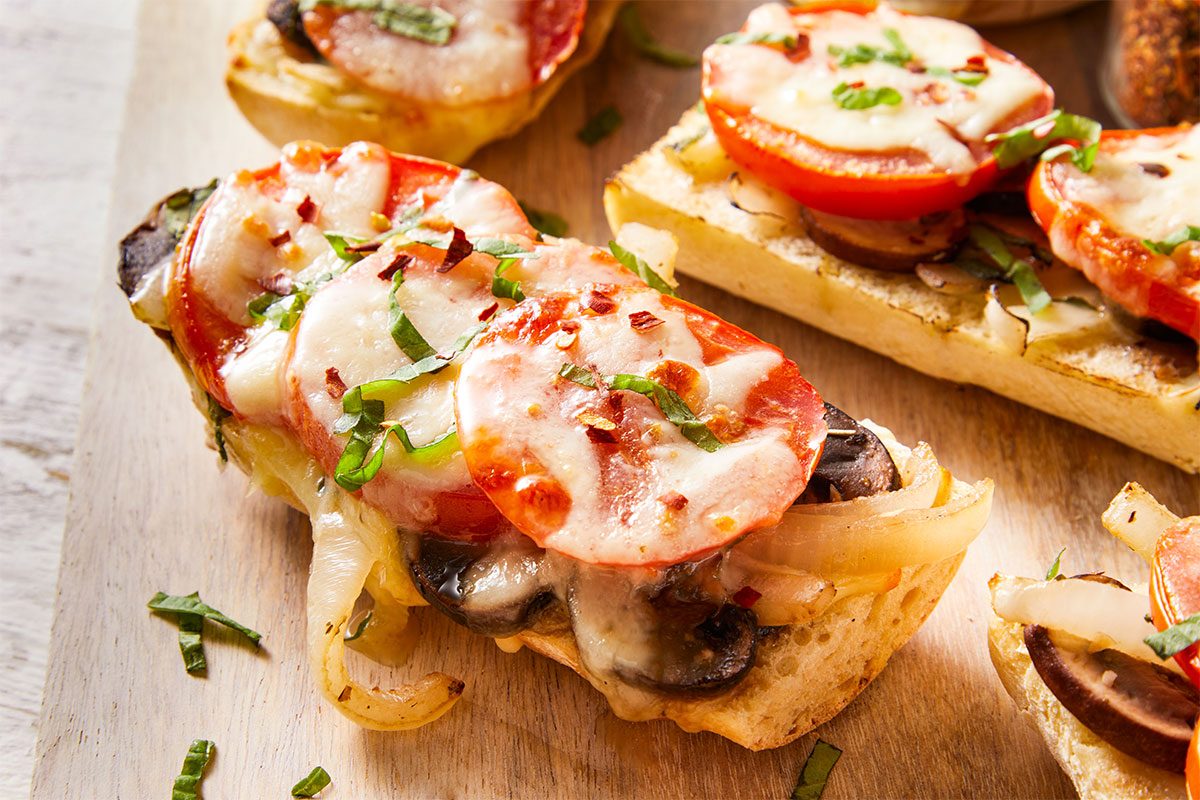 Close-up of Tomato Baguette Pizza showing melted mozzarella and fresh tomato slices with a sprinkle of herbs.