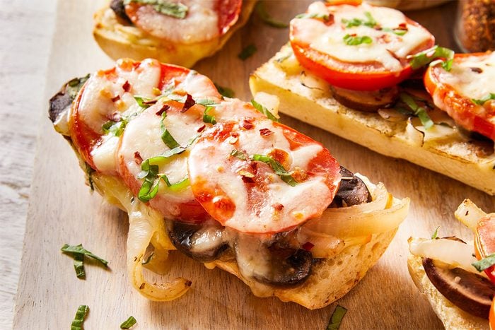 Close-up of Tomato Baguette Pizza showing melted mozzarella and fresh tomato slices with a sprinkle of herbs.