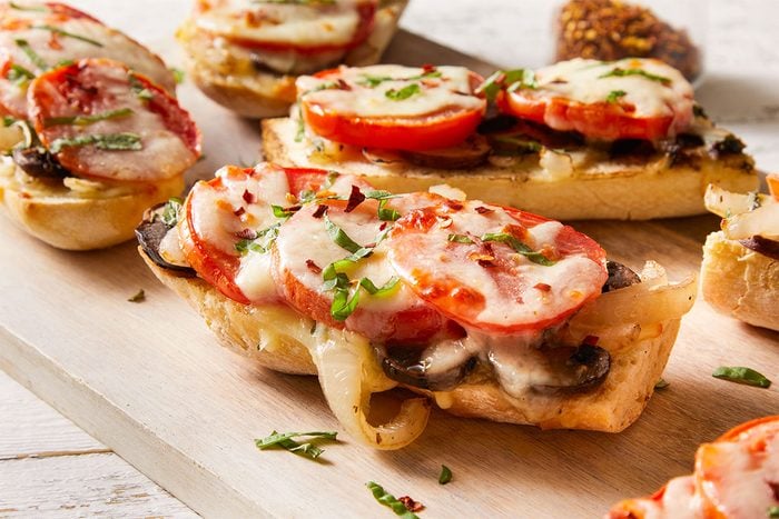 Overhead shot of multiple Tomato Baguette Pizzas arranged on a board, topped with bubbling cheese and fresh herbs.
