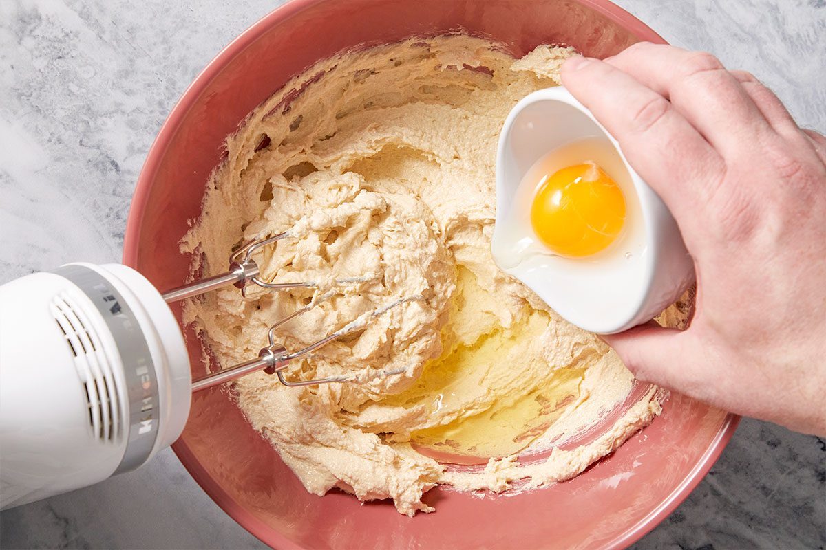Overhead horizontal image of butter and sugar being mixed with eggs added into a mixing bowl.