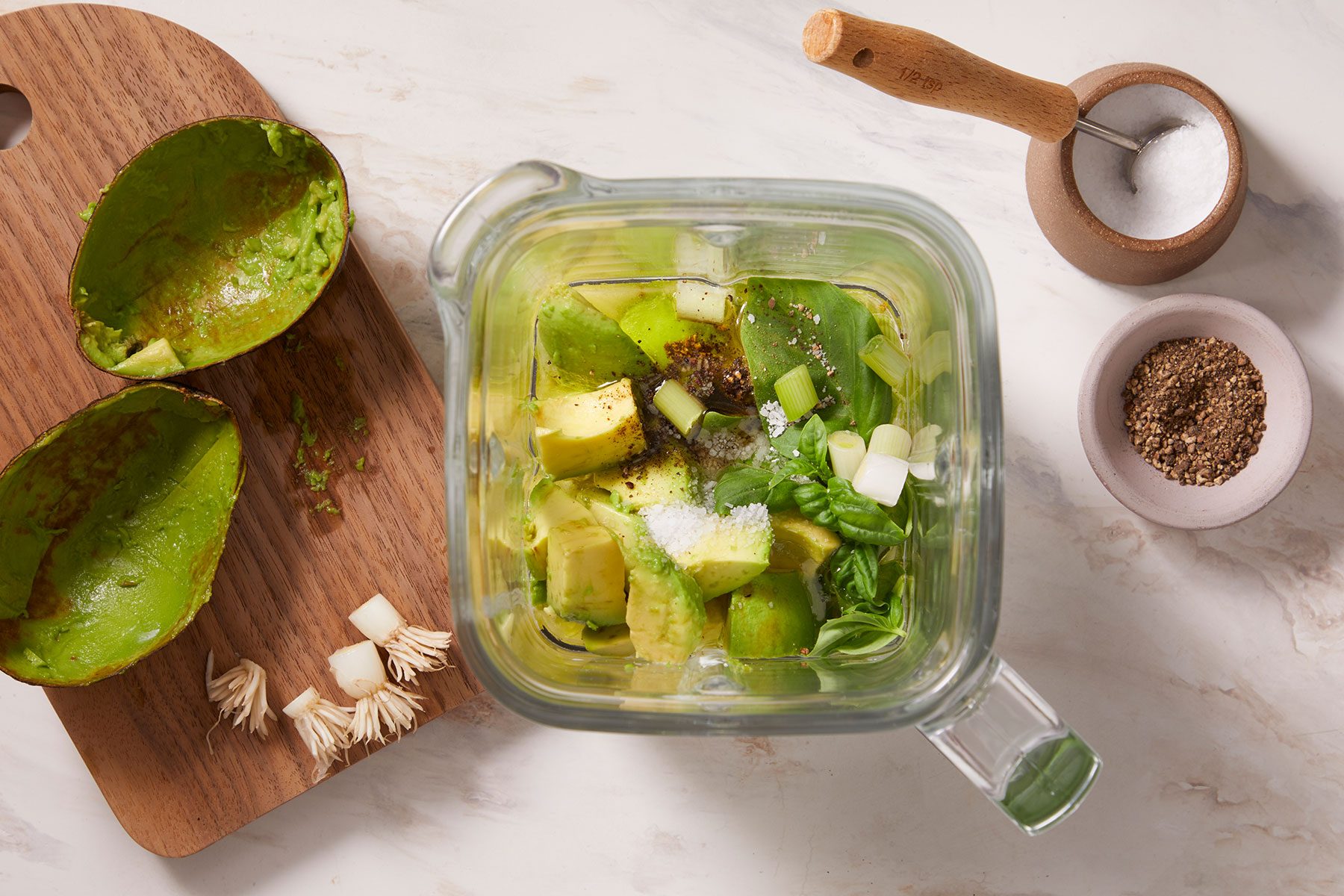 Some olive oil, lemon juice, yogurt, avocado, basil, and green onions in a blender or food processor with salt and pepper on side.
