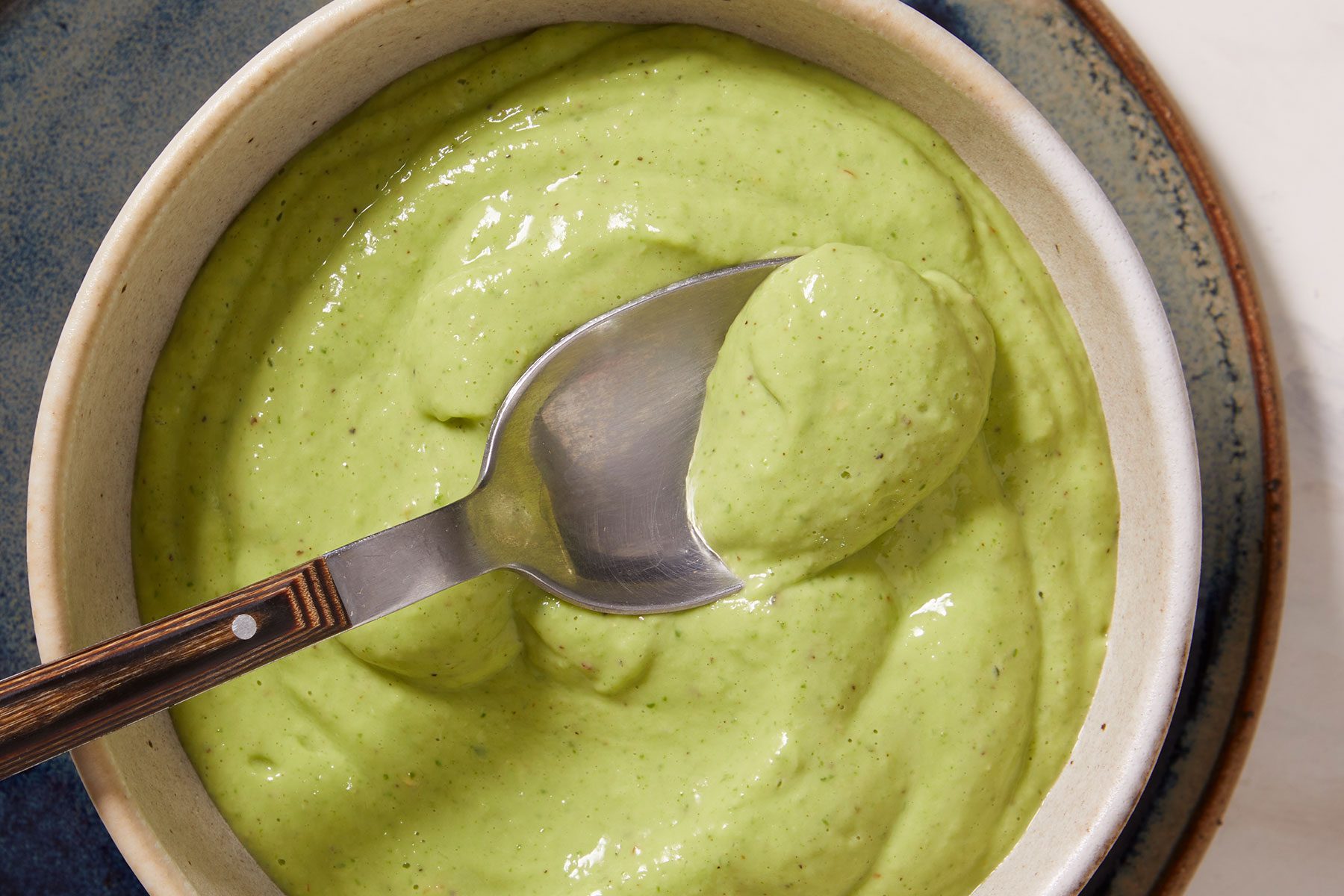 Smooth and creamy Avocado Basil Dressing in a white bowl with a spoon dipped in it.