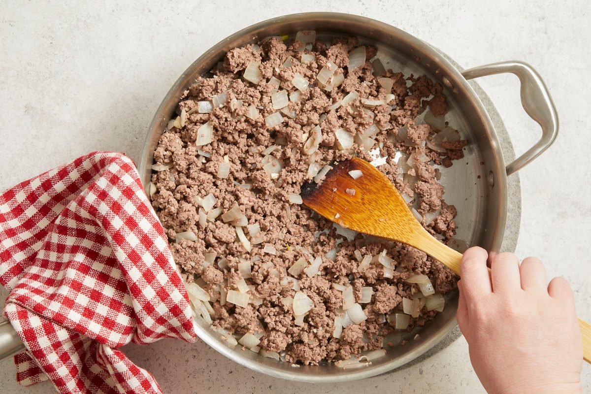 Overhead horizontal step-by-step image of ground beef being browned in skillet with wooden spoon.