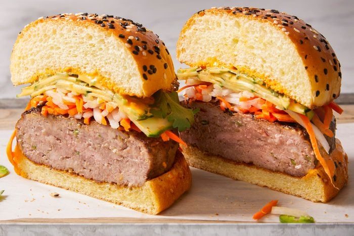Eye Level horizontal image of a cut burger. The halves of the burger show shredded carrots, onions, zucchini, and a sauce between the patty and the seeded bun.