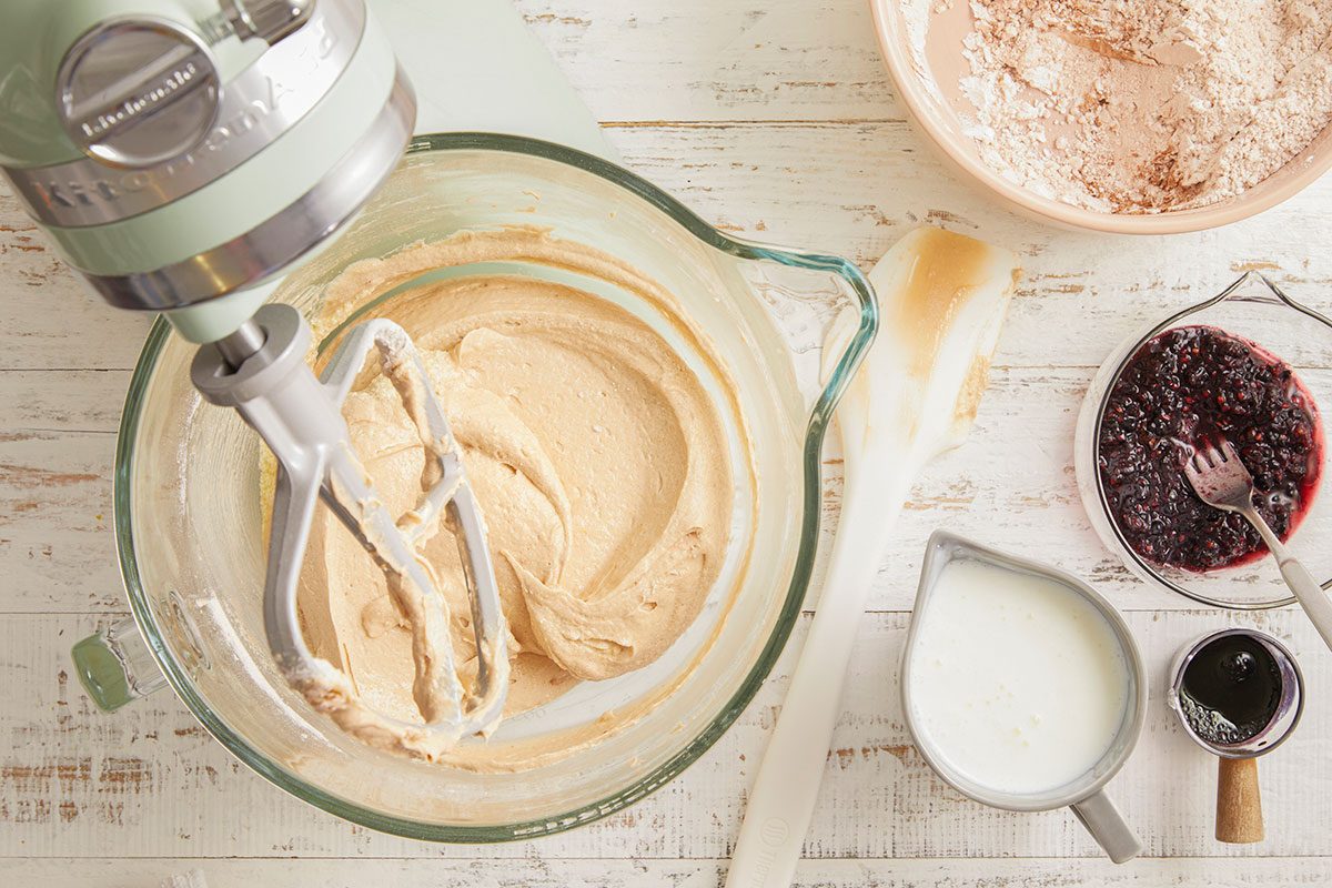 A horizontal image shows a smooth cake batter being mixed with ingredients nearby, including cocoa and buttermilk.