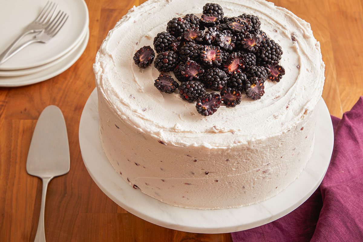 A horizontal image shows a finished blackberry velvet cake topped with fresh blackberries.