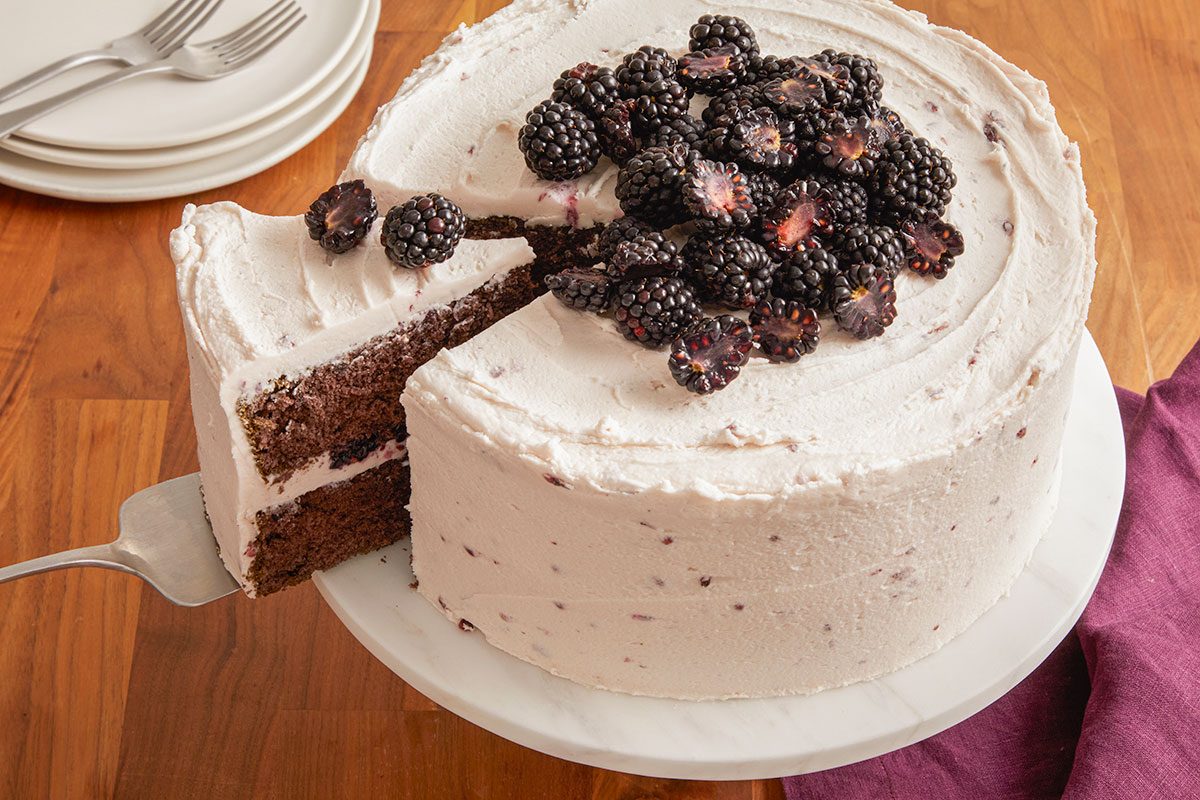 A horizontal image shows the cake with a slice removed, revealing layered blackberry cake and frosting.