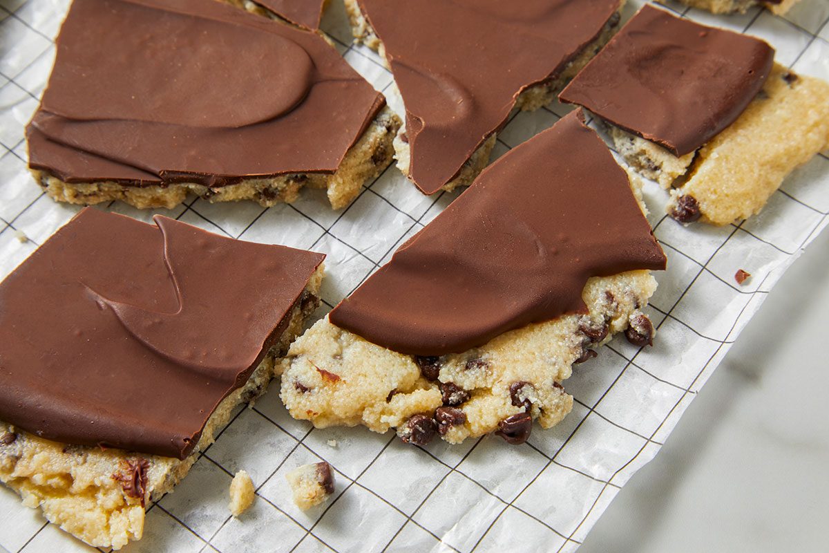 Overhead horizontal image of chocolate chip cookie bars topped with chocolate frosting on a parchment lined baking sheet. The bars are cut into triangle and square shapes and arranged on the baking sheet.
