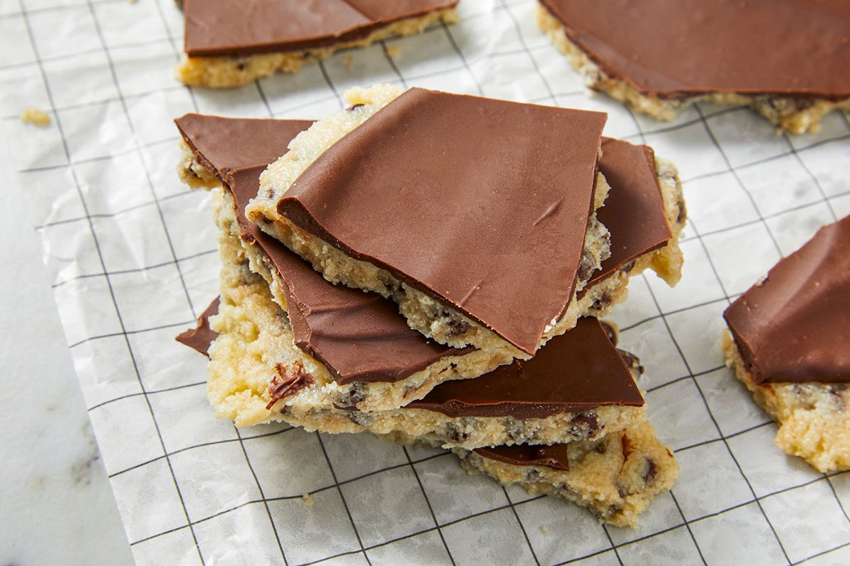 Eye Level horizontal image of several pieces of chocolate chip cookie bark. A stack of the cookie bark is in the center of the image while the rest of the pieces are placed around it on parchment paper.