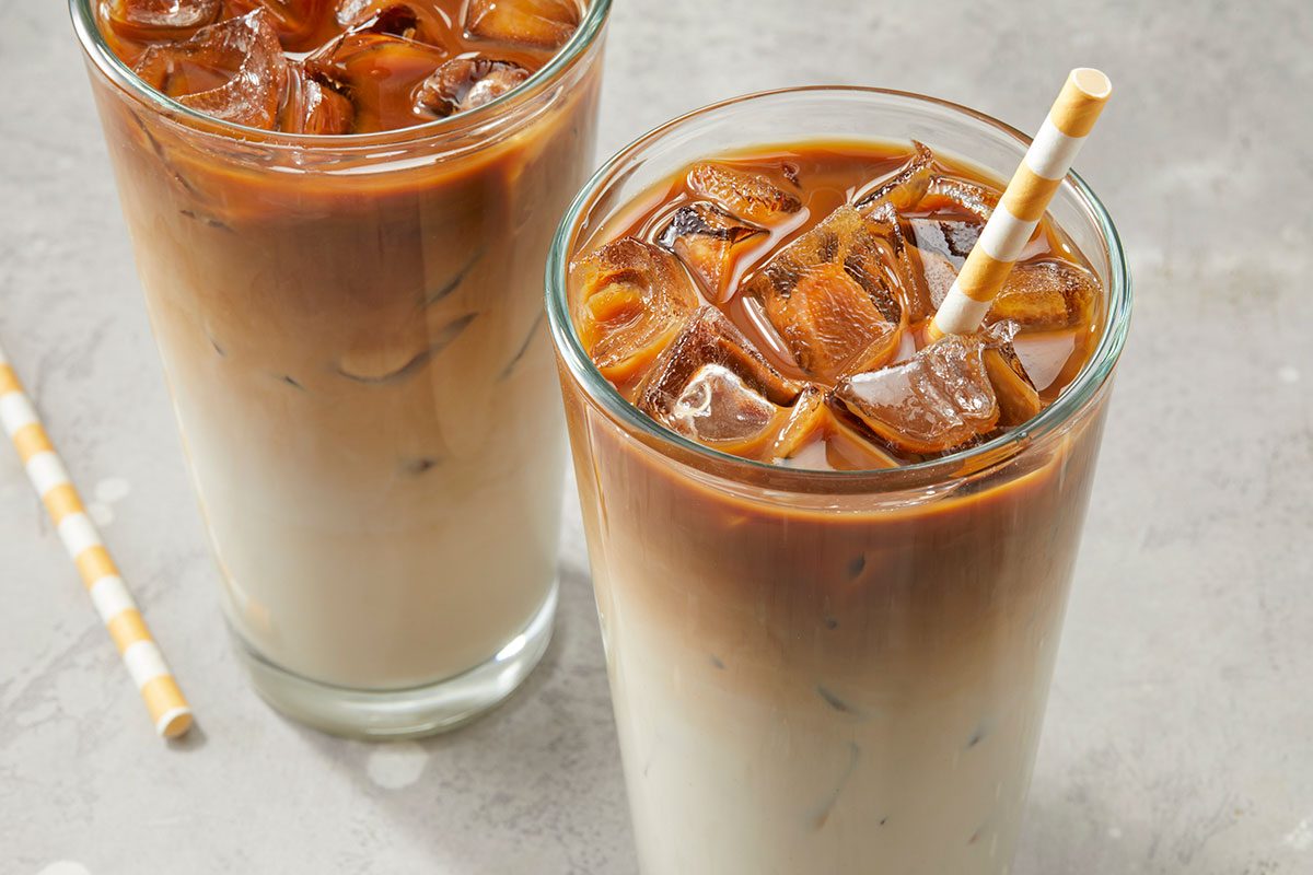 Eye Level horizontal image of two glasses filled with ice, milk, and coffee. One glass has a striped straw in it.