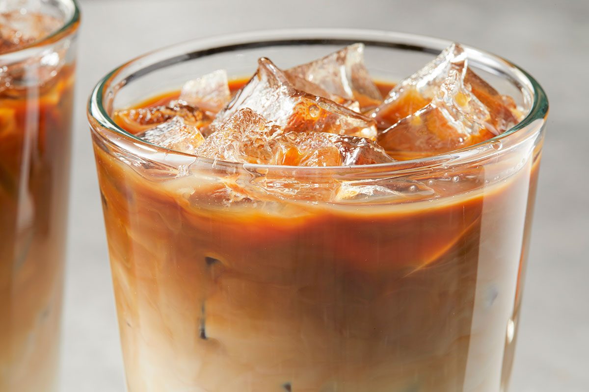 Eye Level horizontal image of a glass filled with ice and iced coffee. A second glass of iced coffee is partially visible in the background.