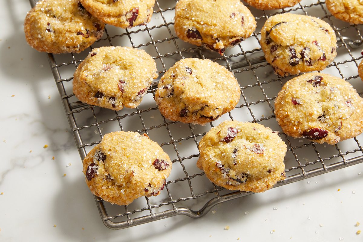 A batch of golden, sugar-coated cookies with chocolate chips sits on a metal cooling rack over a white marble surface.