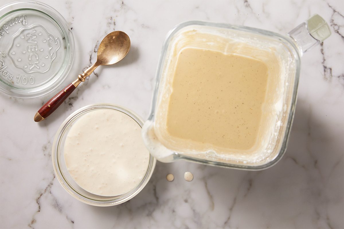 Overhead shot of freshly blended dressing transferred into a storage container, showing its smooth, pale texture on a marble surface.