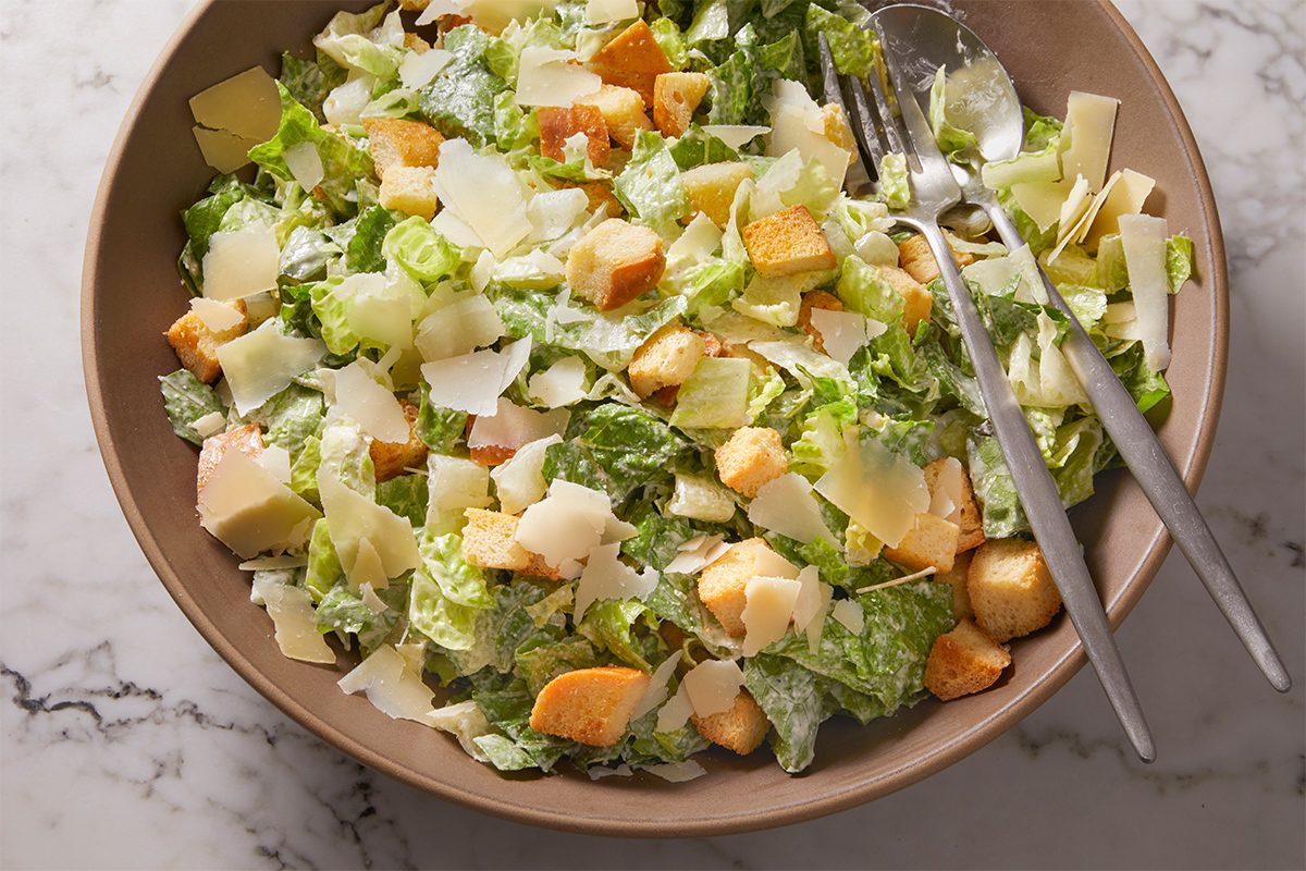 Overhead shot of a Caesar salad tossed with romaine lettuce, croutons, and shaved Parmesan, lightly dressed with creamy Caesar dressing.
