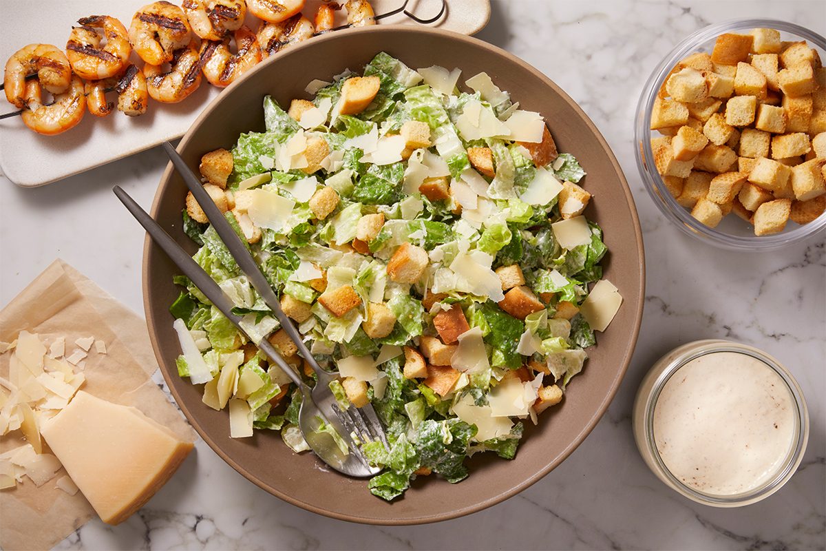 Overhead shot of a Caesar salad tossed with romaine lettuce, croutons, and shaved Parmesan, lightly dressed with creamy Caesar dressing.