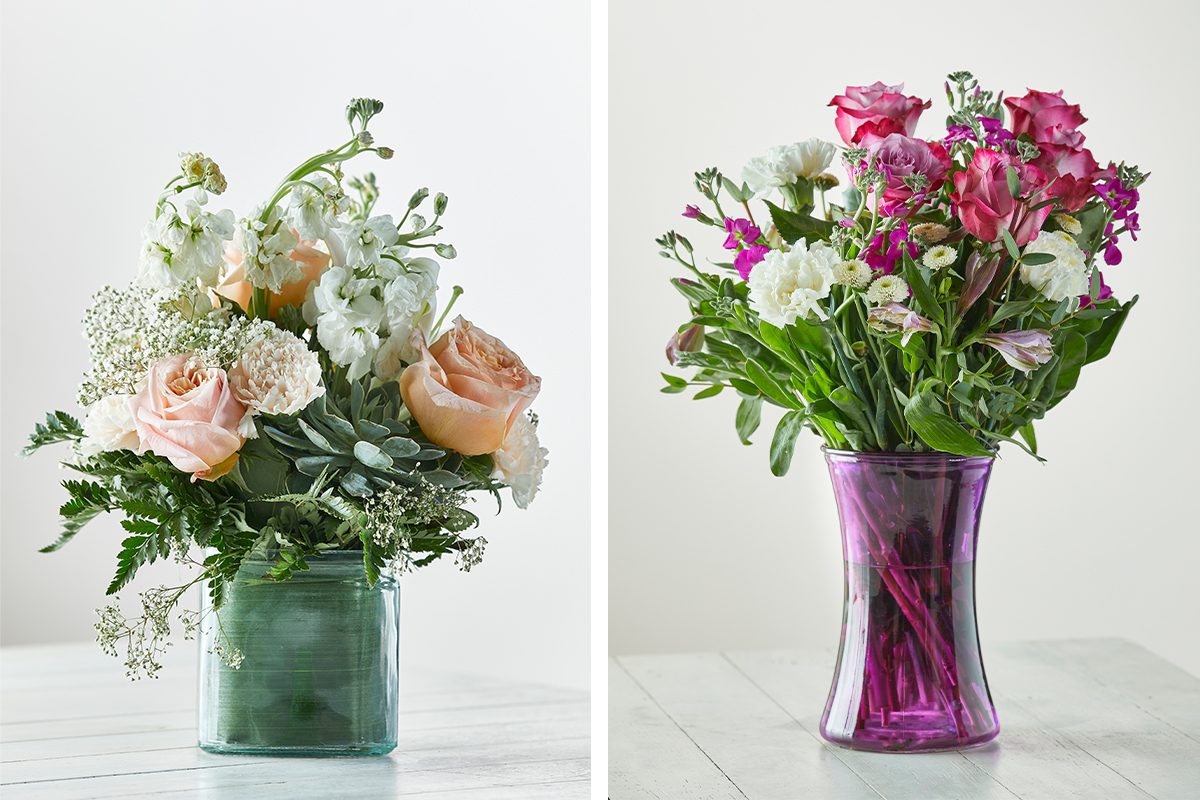 Two glass vases with flower arrangements on a white surface: the left vase is green with light pink and white flowers, while the right vase is purple with vibrant pink and white flowers.