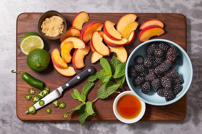 Overhead horizontal image of ingredients prepped on a wooden cutting board. Nectarine slices, blackberries, jalapeno slices, mint sprigs, limes, brown sugar, and honey are visible.