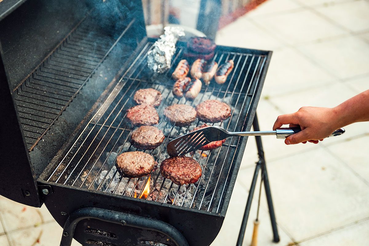 woman cooking on a BBQ, turning over burgers and sausages
