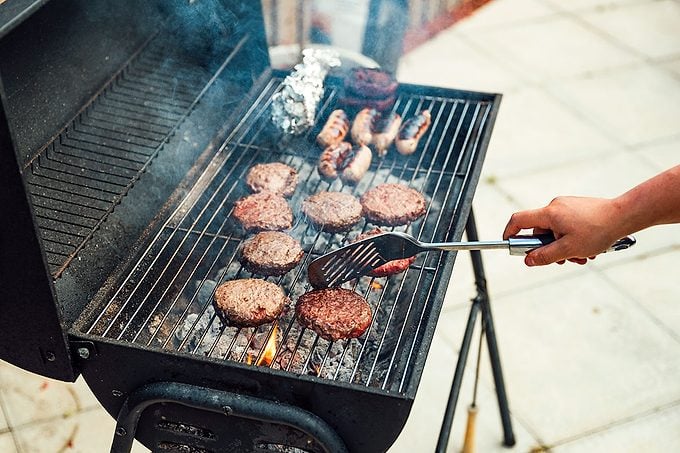 woman cooking on a BBQ, turning over burgers and sausages