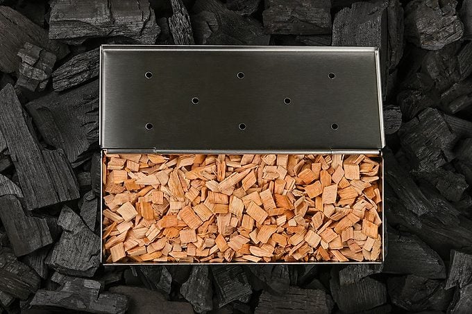 Close up one stainless steel metal smoker box with hardwood alder chips on black lump charcoal pieces, ready to barbecue grill and smoke food