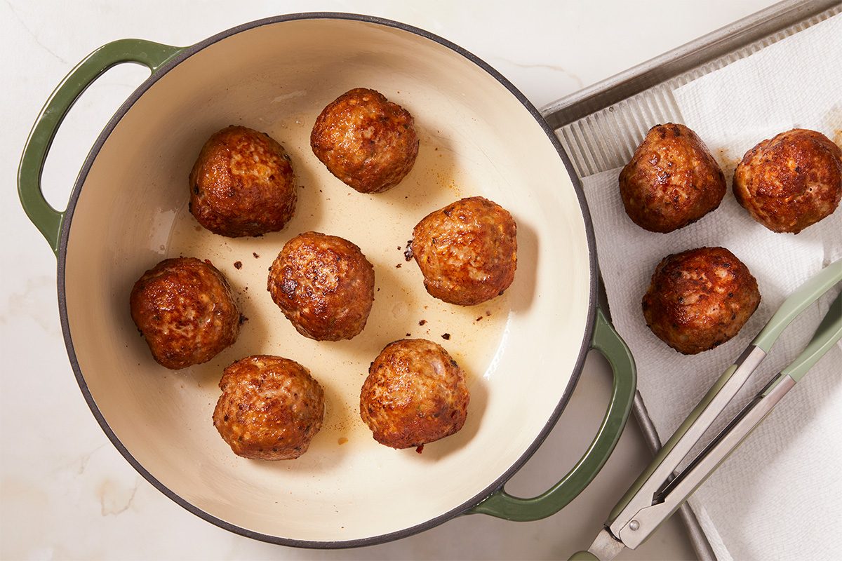 Eye Level horizontal image of a serving platter with multiple meatballs. The meatballs are topped with sesame seeds and green onions, and surrounded by bok choy. A serving of rice is in a bowl in the background.