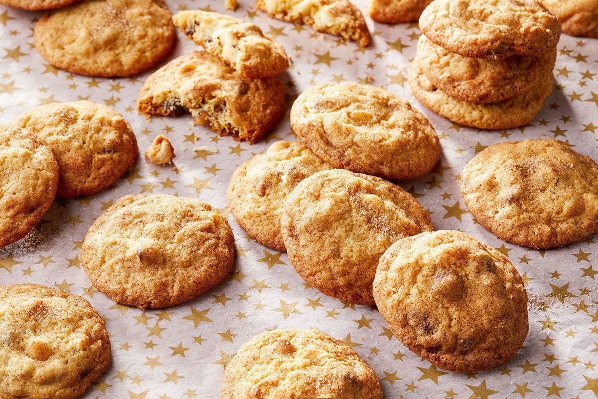 Overhead horizontal image of freshly baked cookies. The cookies are golden brown and covered in granulated sugar and spread out across gold star parchment paper.