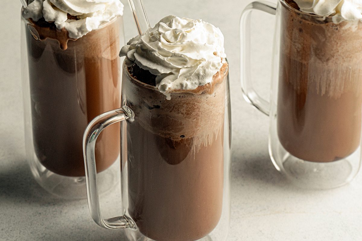3/4 angle view shot of three glass mugs of Old-Fashioned Ice Cream Sodas, each topped with a swirl of whipped cream, placed on a light surface;