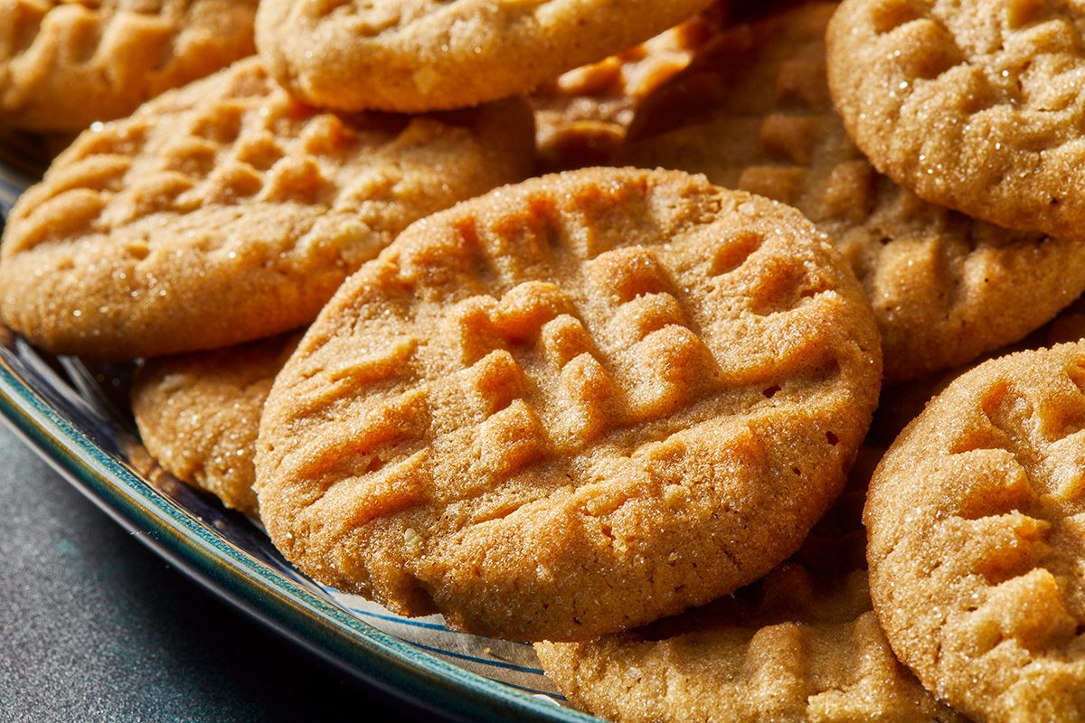 A close-up of a plate filled with peanut butter cookies, each topped with a crisscross fork pattern. The cookies are golden brown and appear soft and freshly baked.